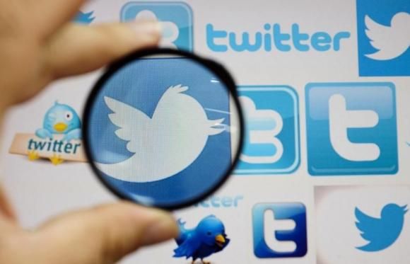 A person holds a magnifying glass over a computer screen displaying Twitter logos