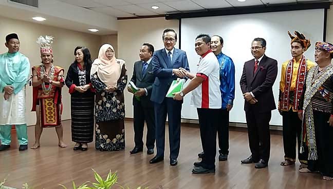 Masidi (in blue suit) handing over a copy of the State Heritage Enactment 2017 book to a representative of a government department in Kota Kinabalu. 