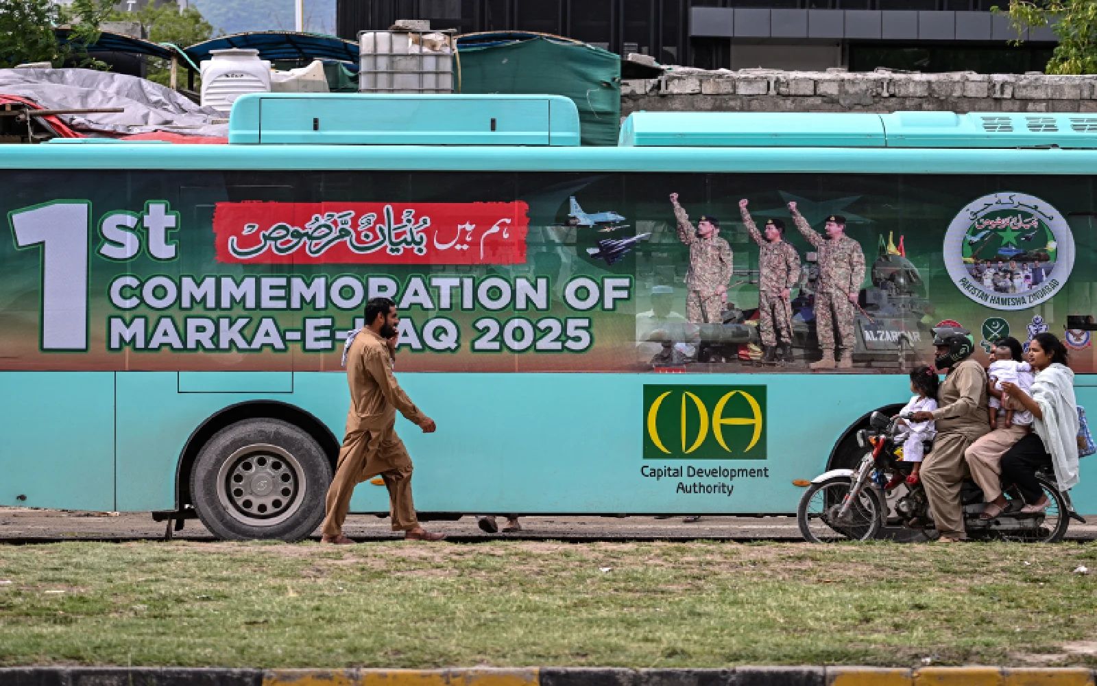 Commuters travel near a government passenger bus carrying a poster of Pakistan's Army Chief and Field Marshal Syed Asim Munir (L) in Islamabad on May 4, 2026 commemorating one year of India-Pakistan clashes after an attack in Indian-administered Kashmir. (Photo by Aamir QURESHI / AFP)